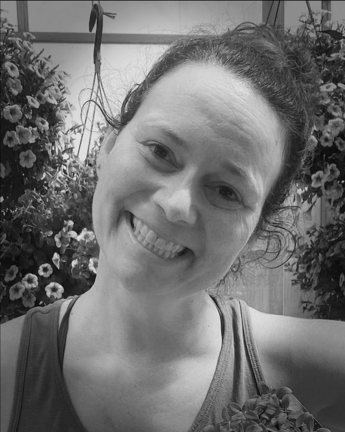 Erin Harward of The Untamed Rose, smiling, among hanging baskets of petunias