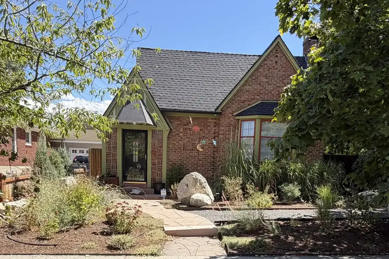 The same brick bungalow with a completed water-wise garden of grasses, shrubs, gravel paths, and boulders