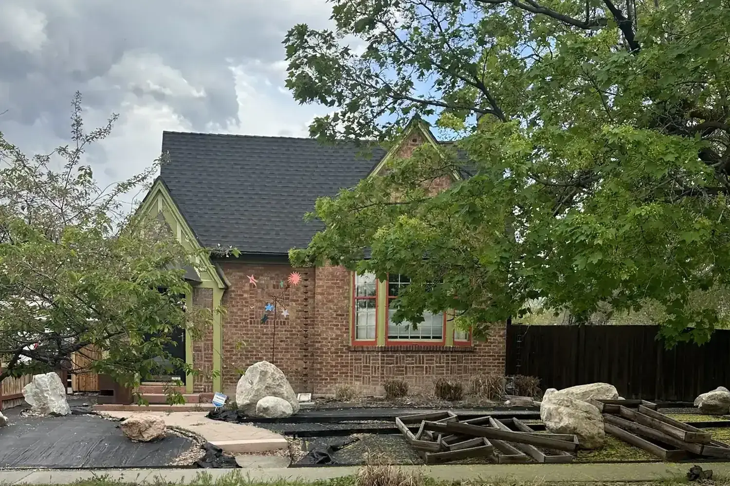 Brick bungalow front yard during installation, with landscape fabric, timber forms, and boulders